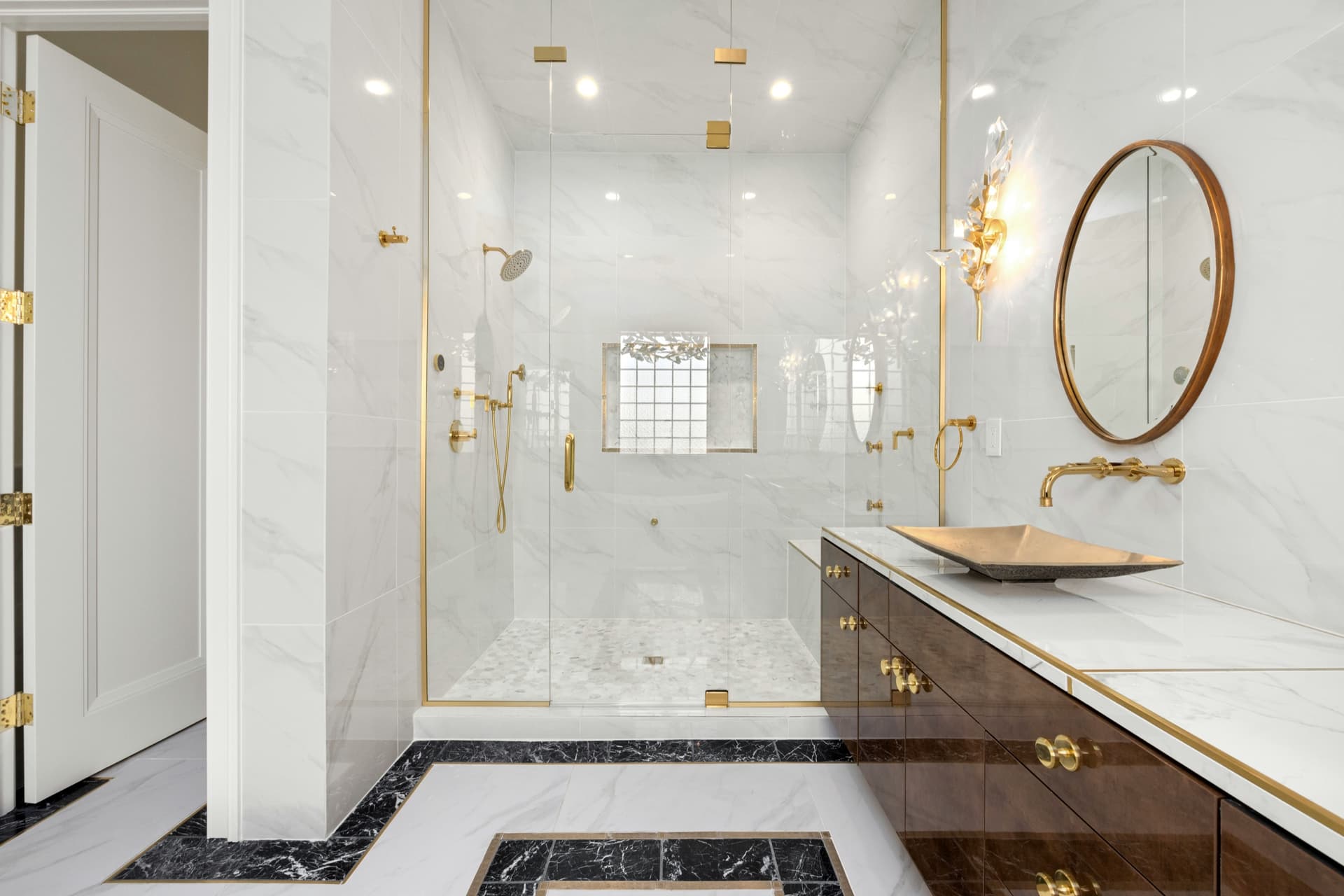 Luxury primary bathroom with marble-look tile, brass fixtures, glass shower, and freestanding tub.