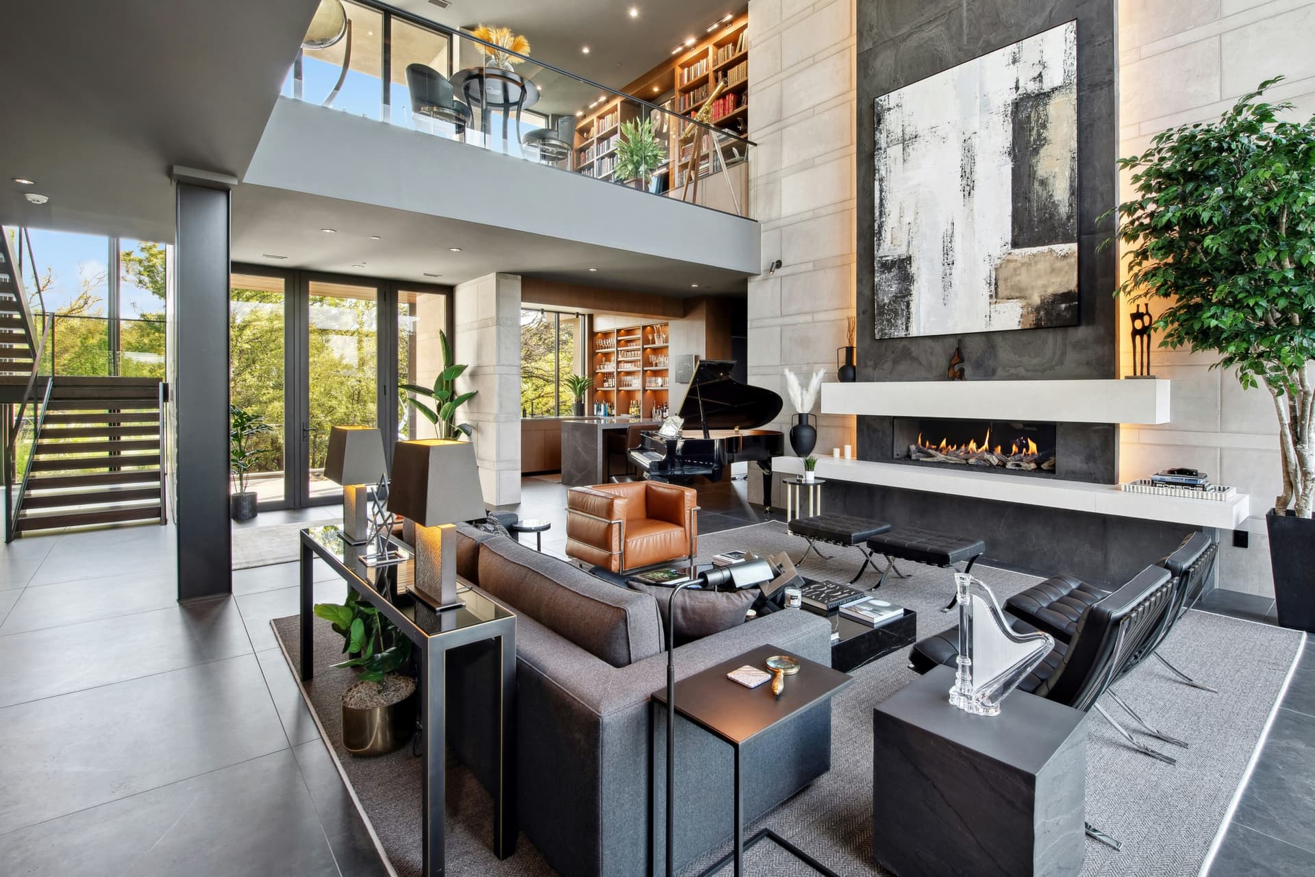 Luxury open living room with fireplace, piano, built-in shelving, and glass rail.