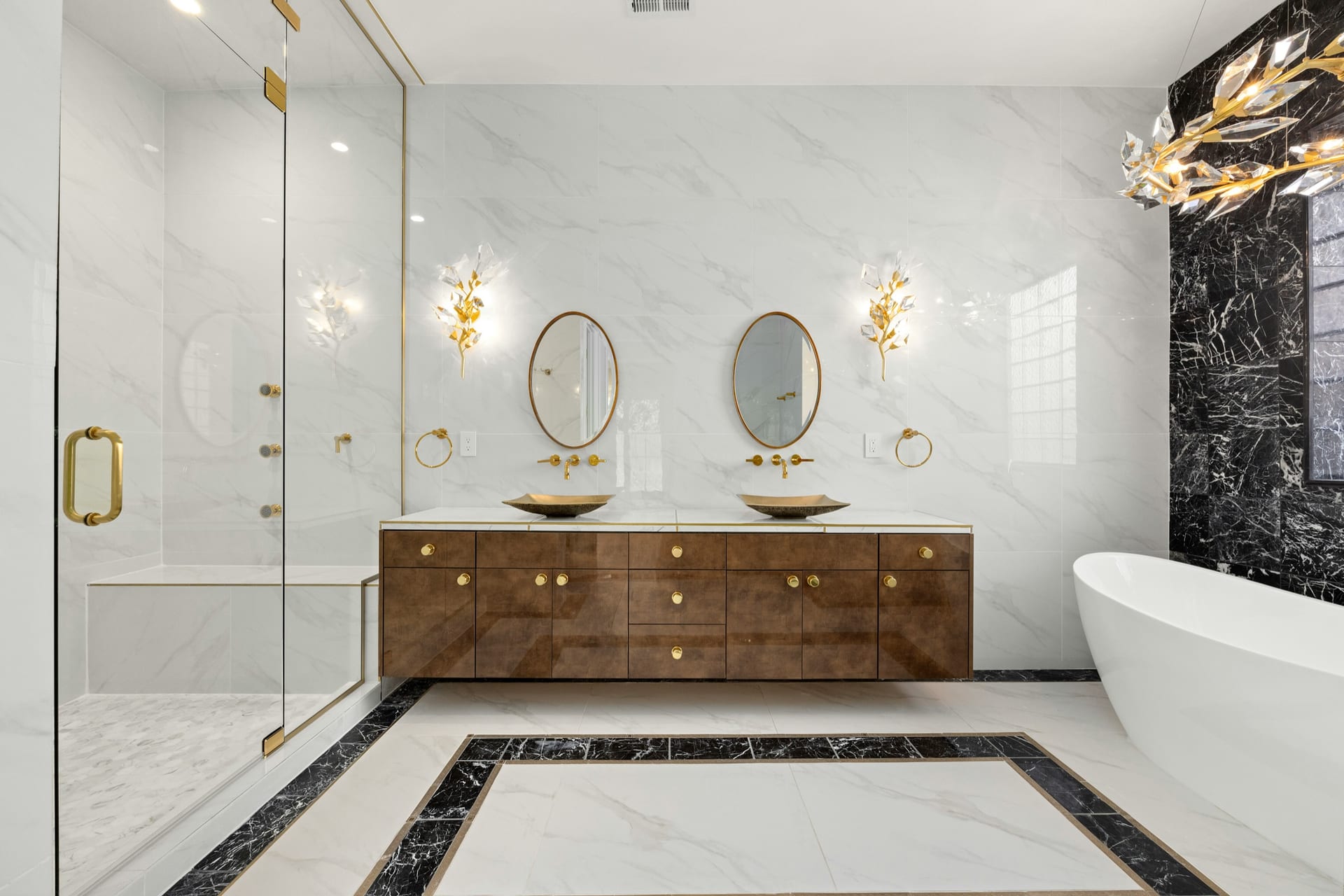 Luxury bathroom remodel with green vanity, marble shower, brass fixtures, and twin mirrors.