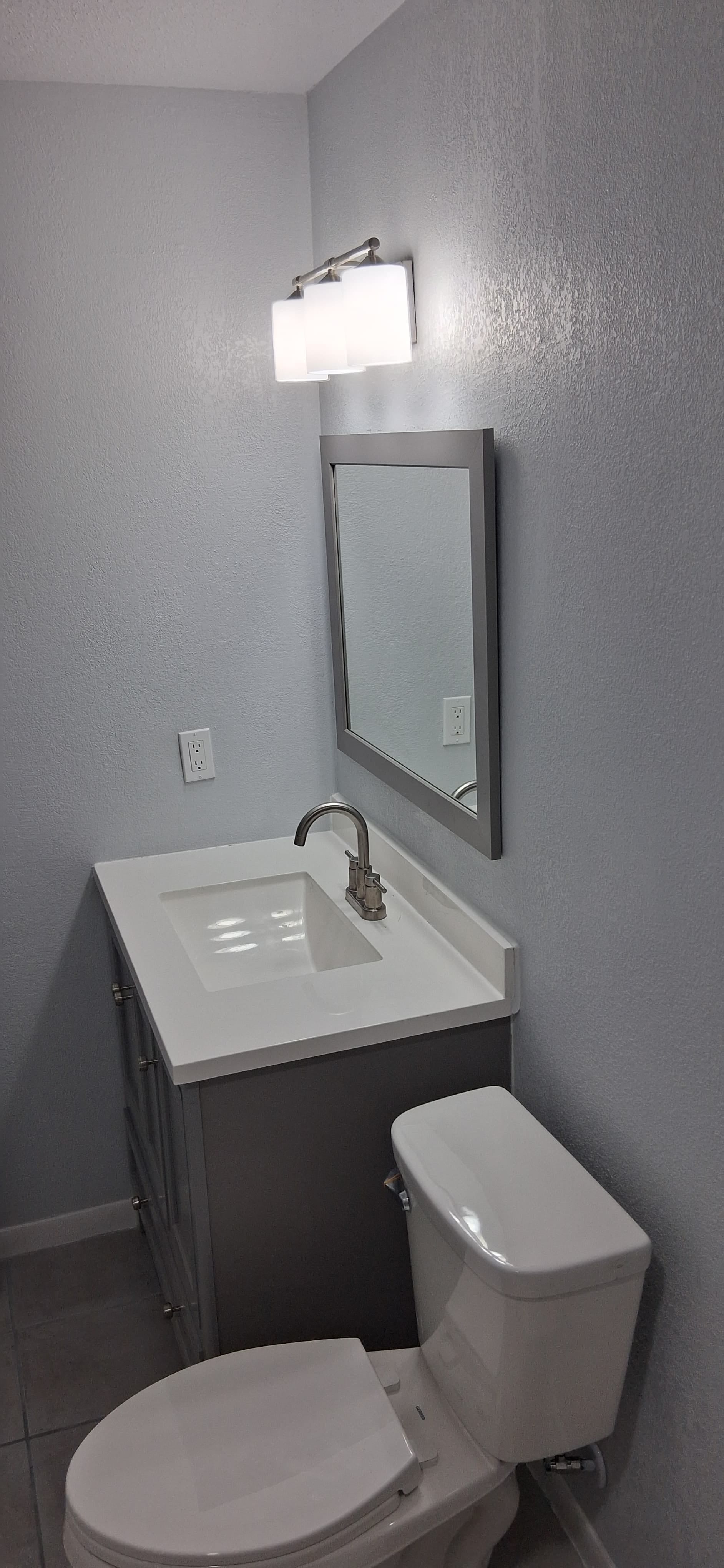 Bathroom vanity, faucet, mirror, light fixture, and toilet installed in a compact bathroom.
