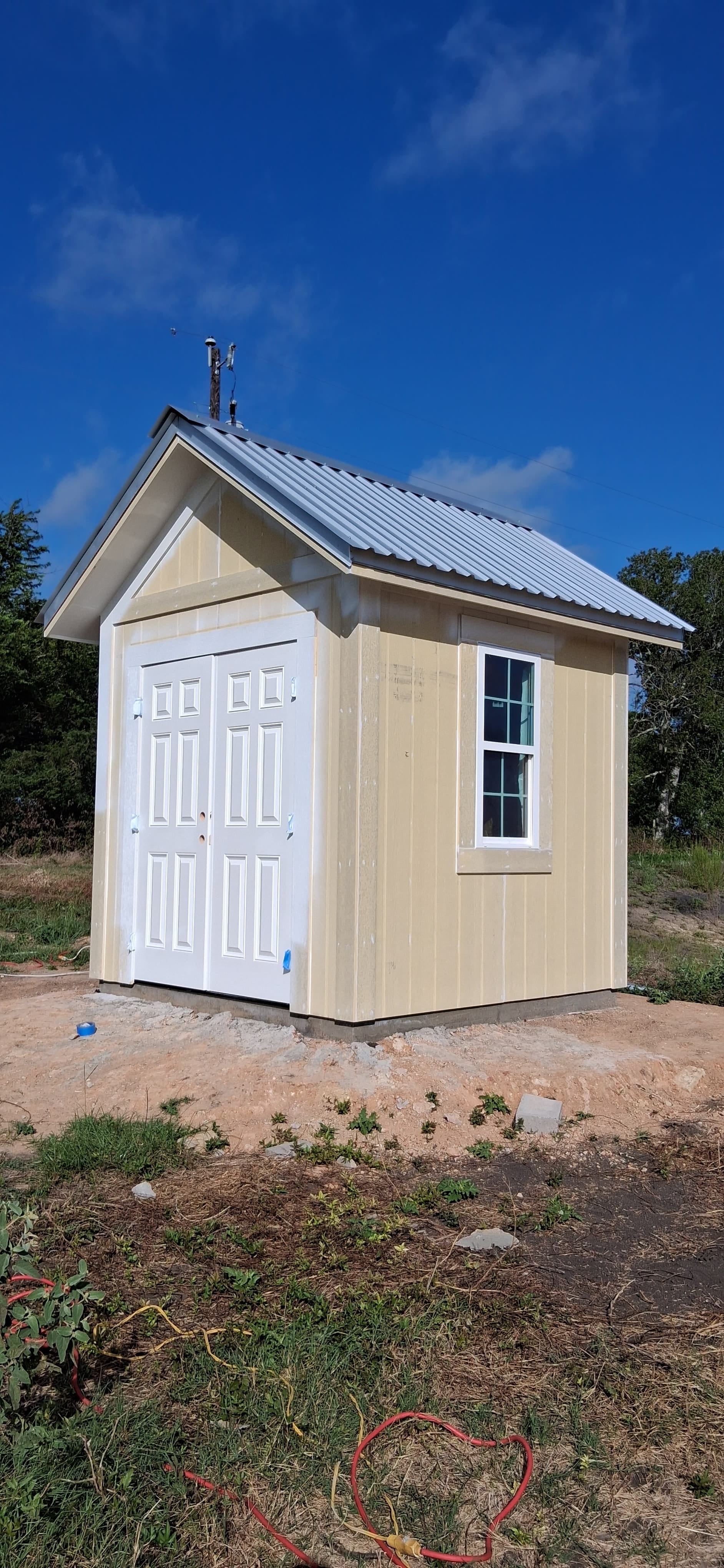 Small exterior structure with fresh siding, white doors, and trim after caulking and painting.