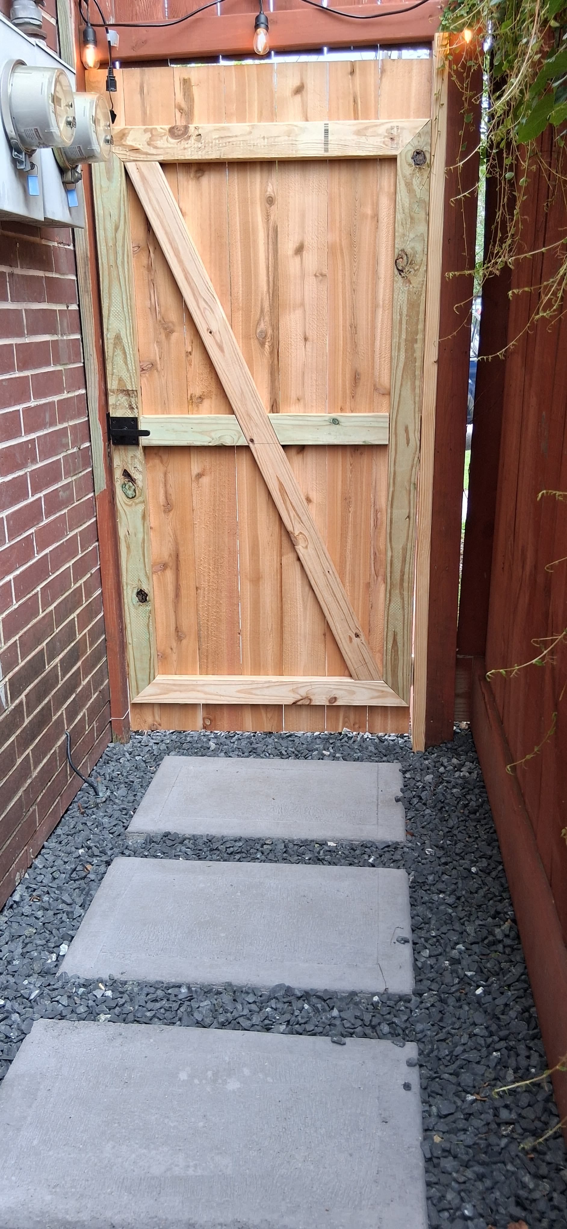 Concrete stepping-stone walkway with gravel leading to a newly built wood gate.