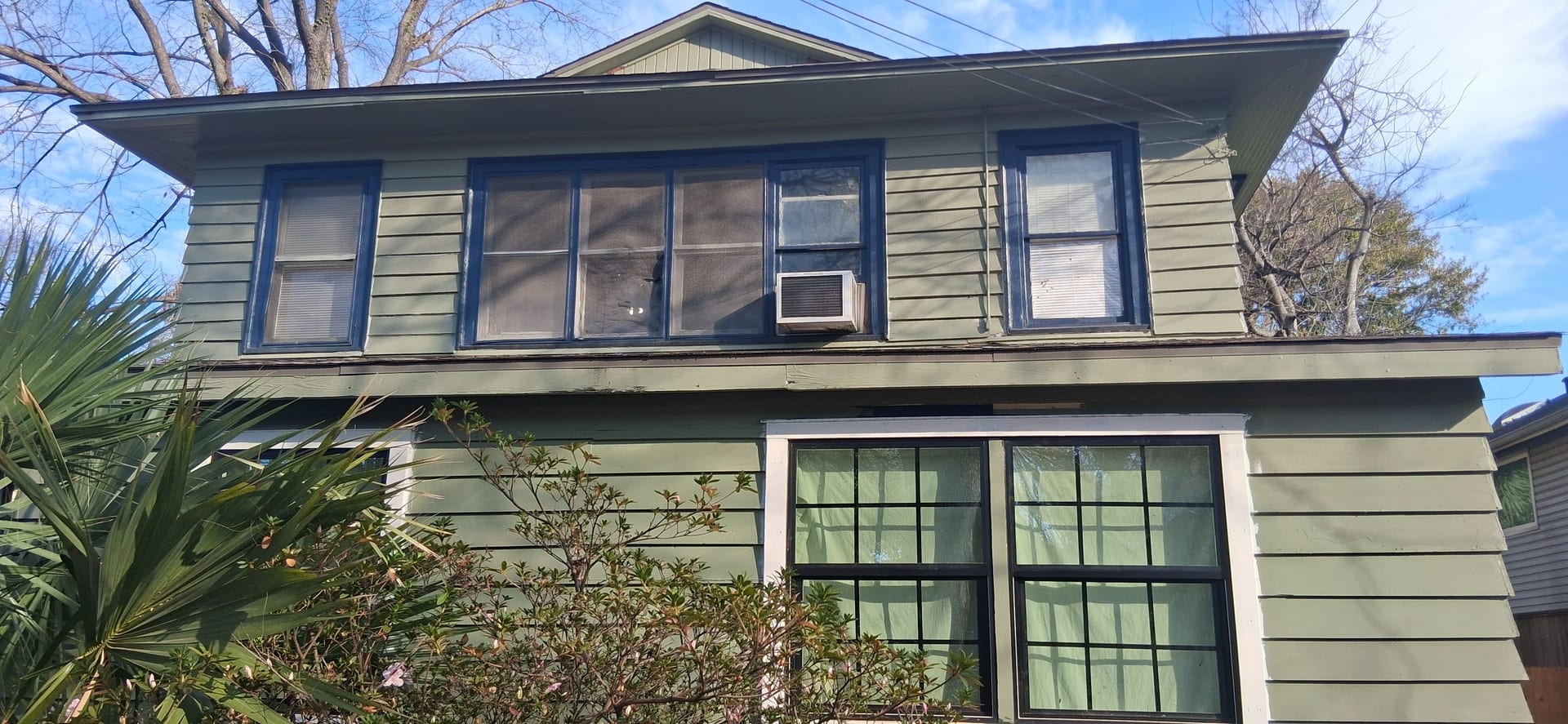 Front of a two-story house showing upper window installation and siding repairs underway.