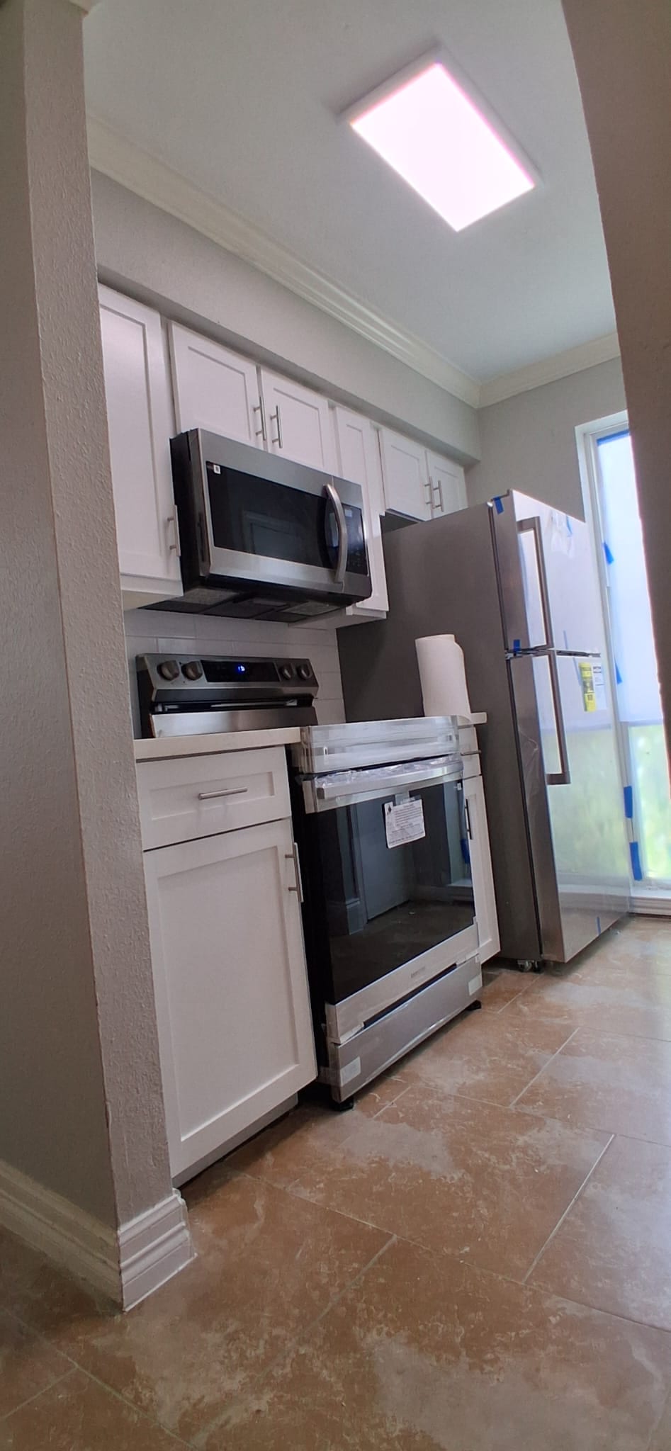 Kitchen with white cabinets, stainless appliances, tile floor, and finish work near completion.