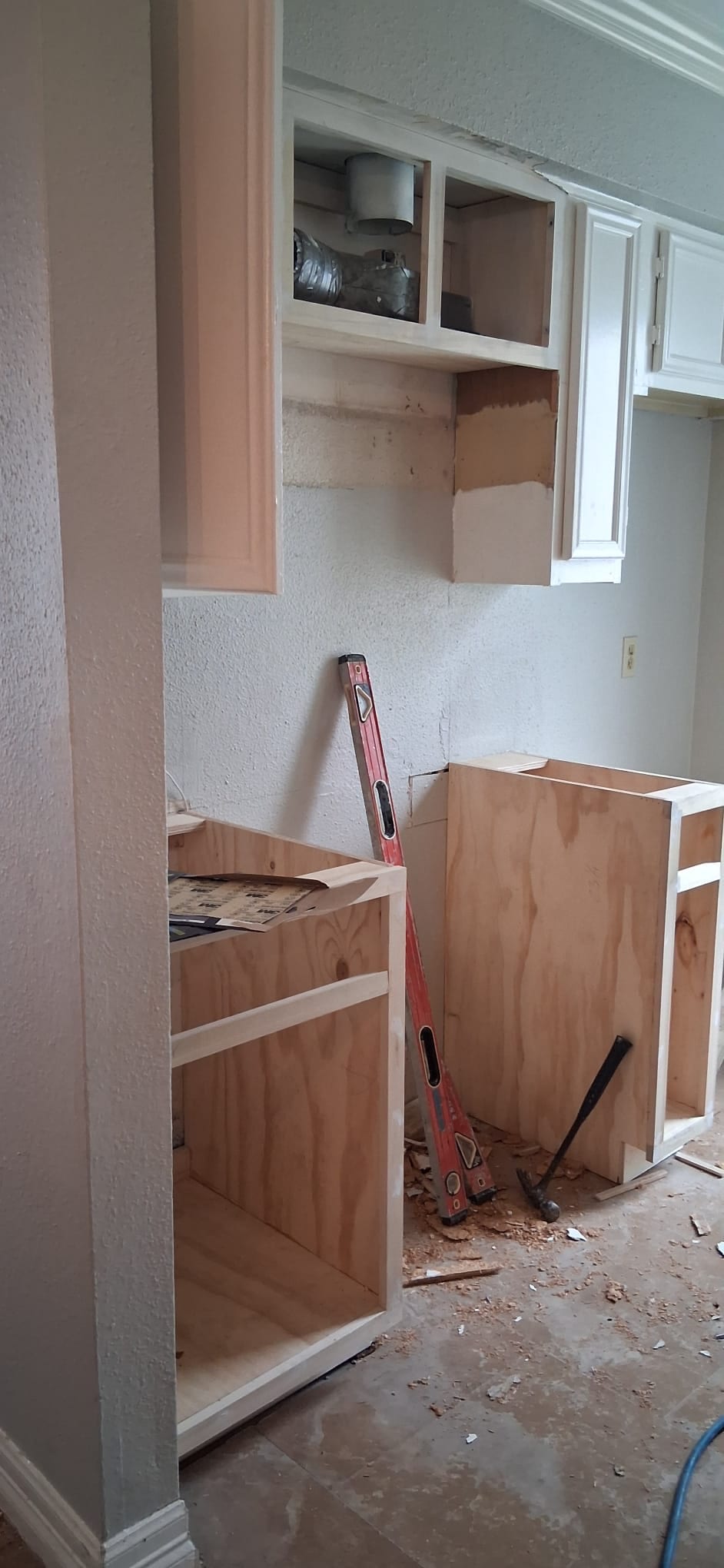 Kitchen remodel in progress with cabinet boxes, tools, and unfinished wall surfaces.