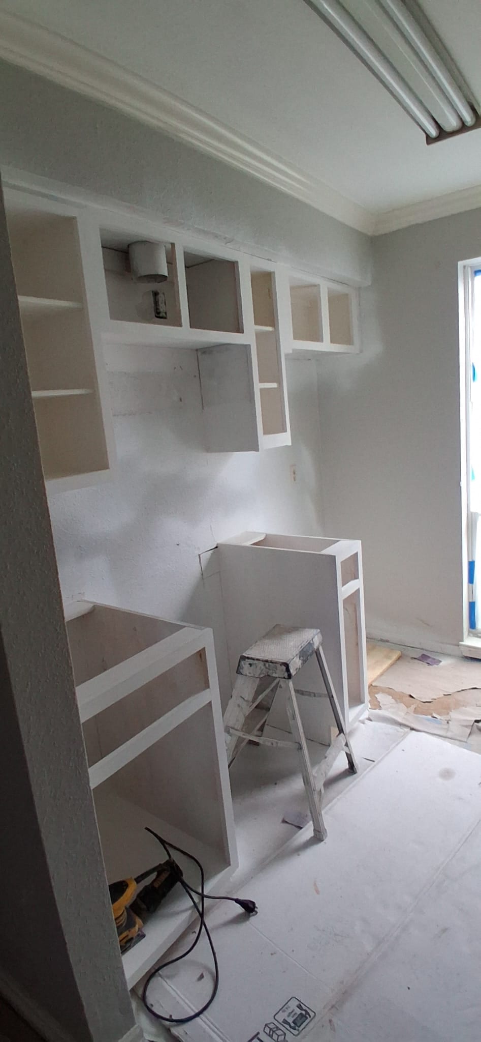 Kitchen cabinet painting and installation work in progress with unfinished lower cabinet area.