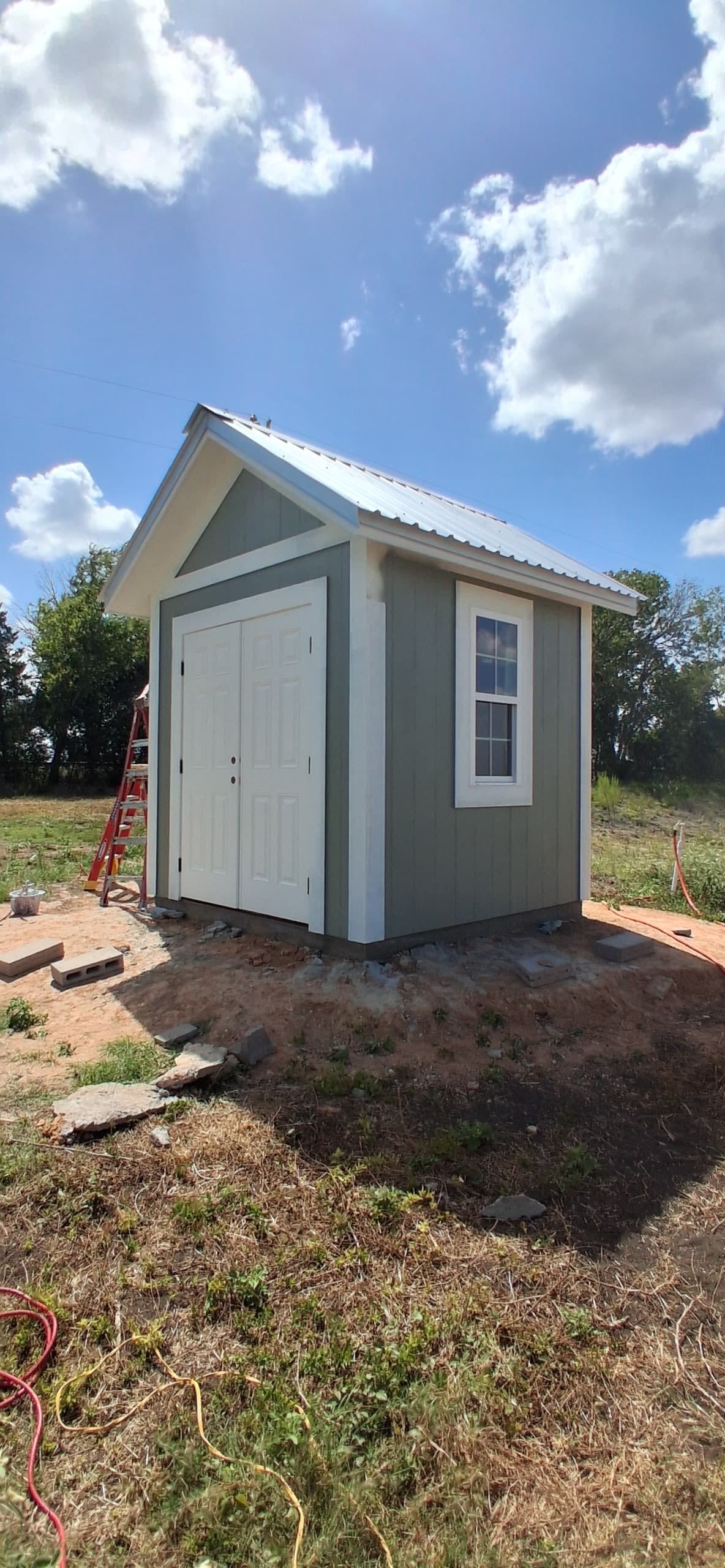 Small painted exterior structure with double doors, trim, and light siding.