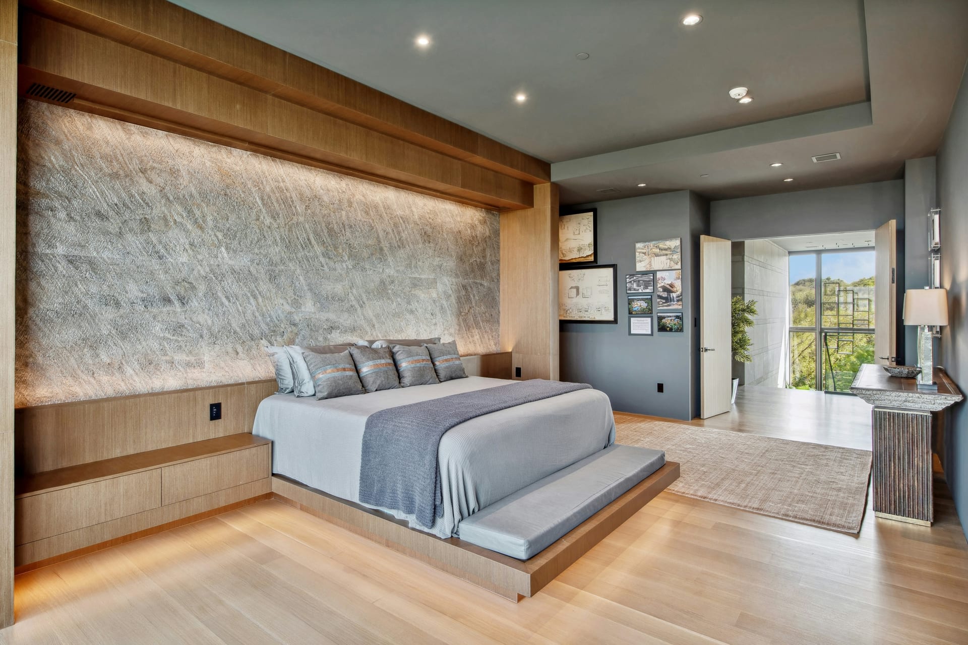 Open-plan remodeled living room with pale wood flooring, custom media wall, and adjacent kitchen.