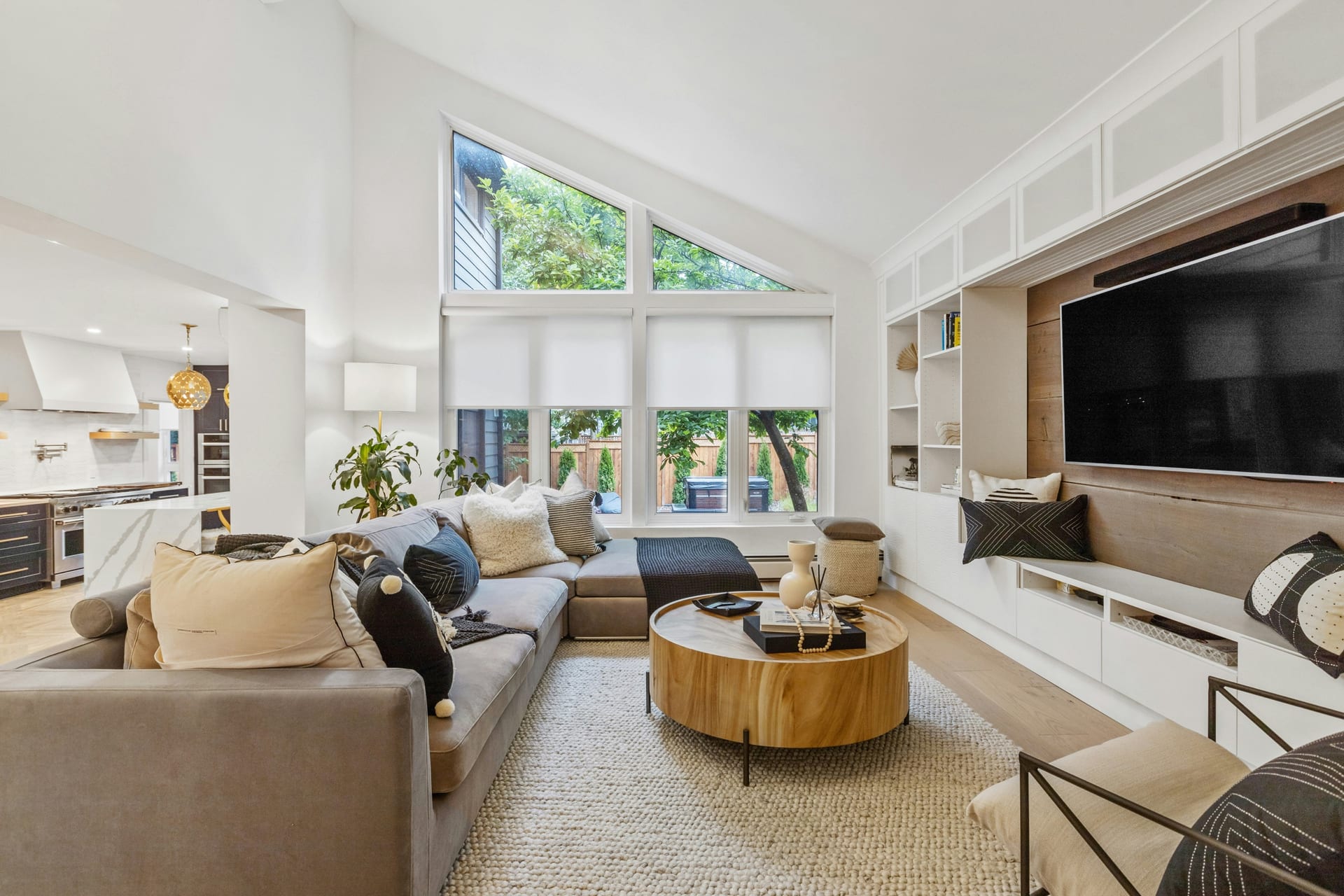 Bright remodeled living area with large windows, custom media wall, and kitchen view.