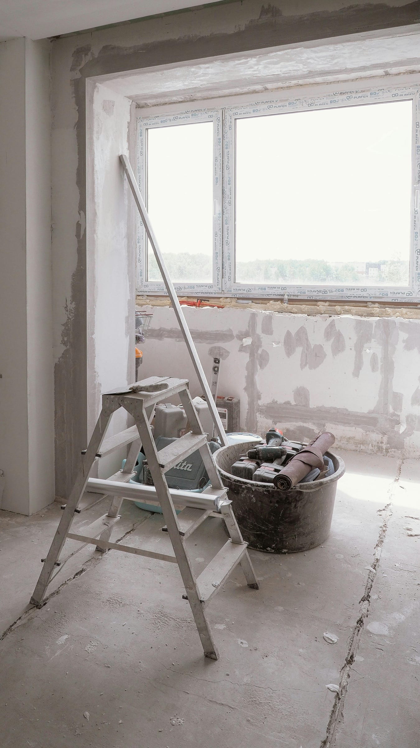 Ladder and tool bucket staged for a repair near a window opening.