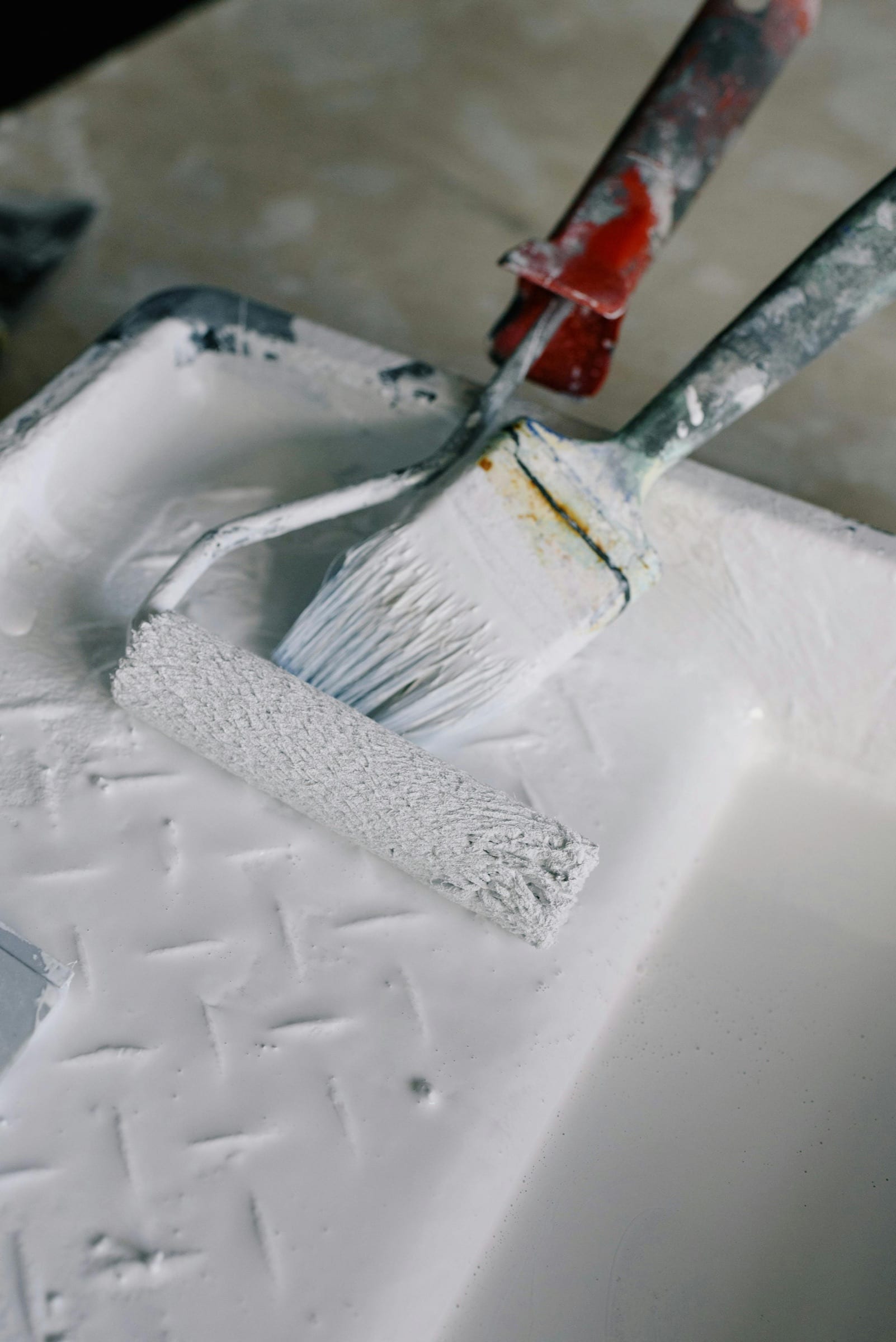 Paint roller and brush resting in a paint tray after a touch-up repair.